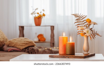 burning candles with autumn decor on white table at home