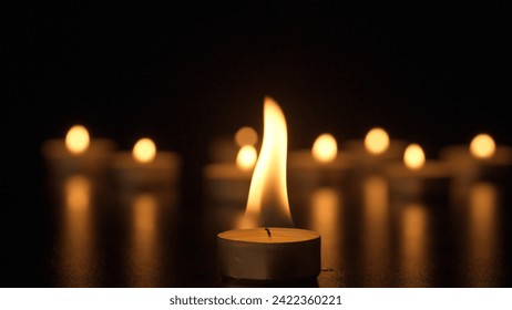 Burning candles. The candles burn against a black background and the flames move when the wind blows. The concept of a memorial day. Background for advertising and design projects. - Powered by Shutterstock