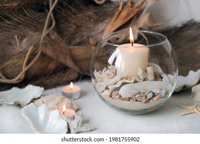 Burning candles in candlesticks decorated in a nautical style with seashells, corals, stones and coconut bark.