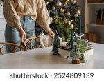 Burning candles with Christmas decor on dining table against woman at home, closeup