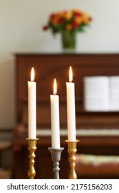 Burning Candles In A Cosy Room Against A Blurry Background. Lighting A Candle Symbolizes Hope And Faith In Religion. Candle Lights In Gold And Silver Holders, For A Wedding, Funeral Home, Or Church