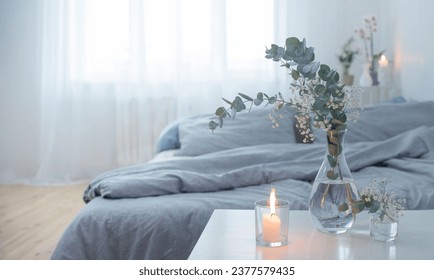 burning candles and eucalyptus in glass vase in white bedroom