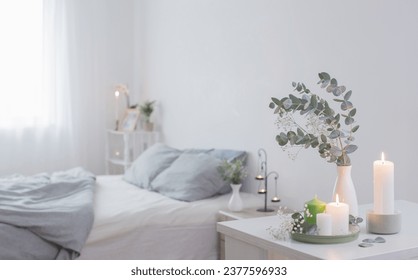 burning candles and eucalyptus in  vase in white bedroom