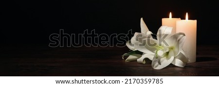 Burning candles and flowers on black background with space for text. Funeral concept