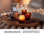 Burning candles, lights, coffee, book and decor on bed indoors, closeup. Autumn atmosphere