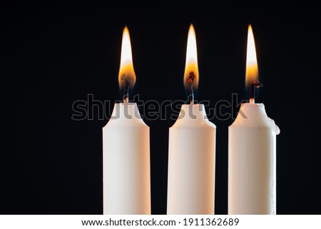 Burning candles on a black background. Three burning wax candles as a symbol of religion. Close-up of candles made of white wax. Concept - sorrow or grief over loss