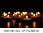 Burning candles on dark surface against black background, closeup