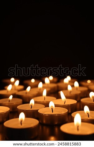 Burning candles on dark surface against black background, space for text