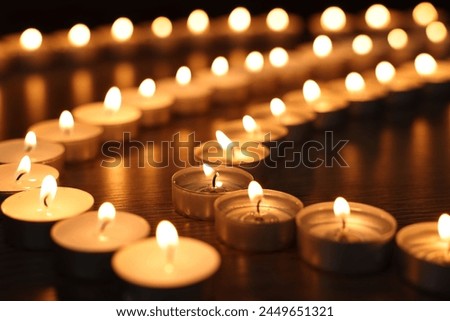 Burning candles on wooden table in darkness, closeup