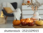 Burning candles and pumpkins on wooden table indoors, space for text. Autumn atmosphere