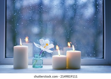 Burning Candles, White Flower In Bottle On Windowsill, Abstract Blurred Raindrops Glass Background. Spring Season. Melancholy Cozy Mood. Relax, Harmony, Meditation, Life Balance Concept. Rainy Weather