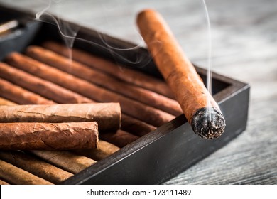 Burning Cigar With Smoke On Old Humidor