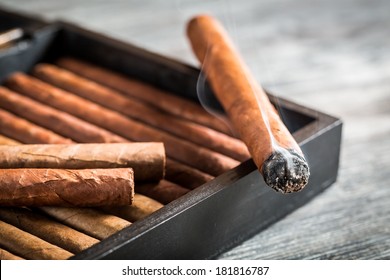 Burning Cigar With Smoke On Wooden Humidor