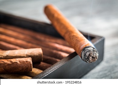 Burning Cigar With Smoke On Wooden Humidor