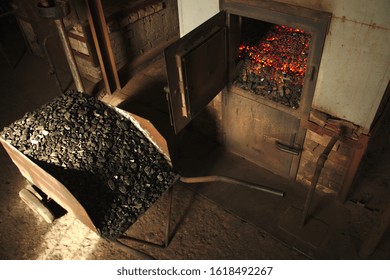 Burning Coal In The Furnace. A Coal-filled Cart Stands Near The Stove.