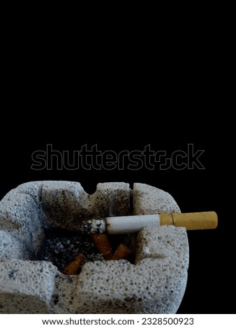 a burning filter cigarette above an ashtray on a black background