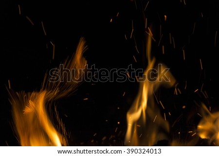 Burning fire with fiery orange flames, sparks and embers exploding into the air on a dark background with copy space