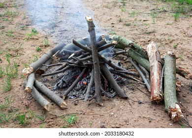 A burning fire on the sand. Make a fire in nature. Smoke from a dying fire. A campfire in the form of a hut. Harvesting wood for the fire. - Shutterstock ID 2033180432