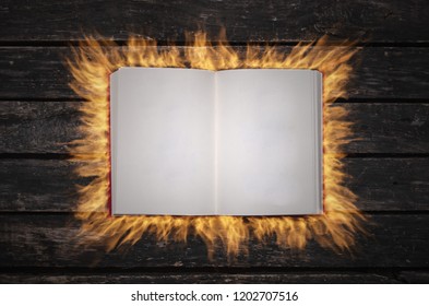 Burning with fire an open magic book with empty blank pages on the table.