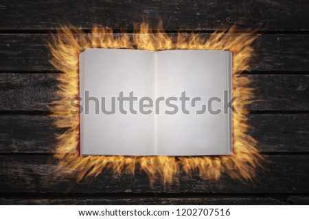 Burning with fire an open magic book with empty blank pages on the table.