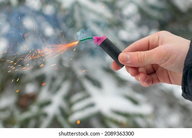 Burning Firecracker in a Hand. Guy Holding a Petard Outdoors in Winter at Daytime. Loud and Dangerous New Year's Entertainment. Hooliganism with Pyrotechnics. Noise of Firecrackers in Public Places