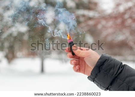Burning Firecracker in a Hand. Guy Holding a Petard Outdoors in Winter at Daytime. Loud and Dangerous New Year's Entertainment. Hooliganism with Pyrotechnics. Noise of Firecrackers in Public Places