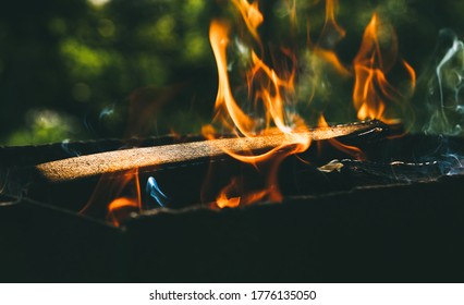 Burning firewood in a homemade barbecue on background of green foliage in garden. Firewood, fire and smoke close-up - Powered by Shutterstock