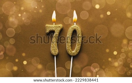 Burning golden glitter number 70 celebration candle on brown bokeh background