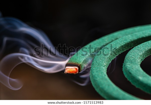 Burning green spiral mosquito\
repellent coil and red fire  with white smoke on dark\
background.