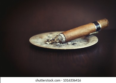 Burning handmade luxury Cuban cigar resting on an ashtray on an old wooden countertop in a nightclub or bar with copyspace - Shutterstock ID 1016336416