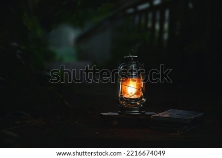 A burning light, a red lamp and a book brightly illuminate a dark night forest road
