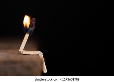 Burning match human sitting on wooden table on a dark background.