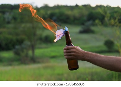 Burning Molotov cocktail on blurred background of hand of white Caucasian young man or adult guy in casual wear. A medical surgical mask is used as a wick. - Shutterstock ID 1783455086