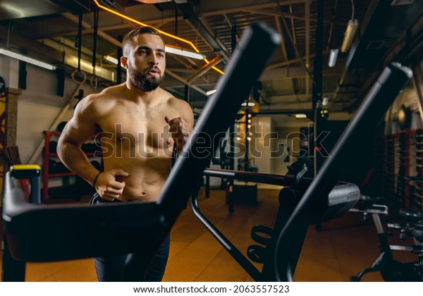 Burning off calories. Maintaining health, motivation.\
Portrait of young sportive man running on a treadmill. Doing\
cardio. Concept of sport, health, action, nutrition. Copy space for\
ad