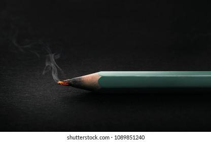 Burning pencil tip glowing on dark background