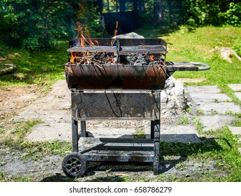 Burning And Preheating Old Rusty Barbecue Grill Cleaning Dirty Grid. Flames In Bbq In Nature - Outdoors Picnic. Preparing The Barbecue For Charcoal On Backyard.