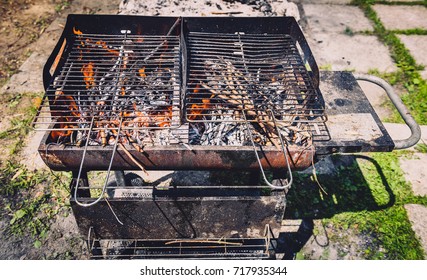 Burning And Preheating Old Rusty Barbecue Grill Cleaning Dirty Grid. Flames In Bbq In Nature - Outdoors Picnic. Preparing The Barbecue For Charcoal On Backyard.