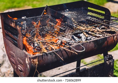 Burning And Preheating Old Rusty Barbecue Grill Cleaning Dirty Grid. Flames In Bbq In Nature - Outdoors Picnic. Preparing The Barbecue For Charcoal On Backyard.