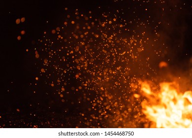Burning red hot sparks fly from big fire. Beautiful abstract background on the theme of fire. Burning coals, flaming particles flying off against black background.