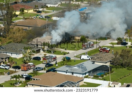 Burning residential house on fire with smoke and flames and firefighters extinguishing it after short circuit spark ignited wooden roof damaged by hurricane Ian. Home disaster in Florida rural area