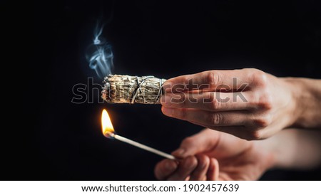 Burning a sage smudge stick for smudging or space cleansing ceremony, black background