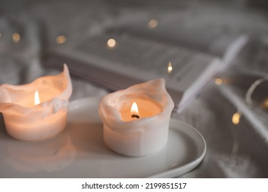 Burning Scented Candles On White Ceramic Tray With Open Paper Book In Bed Close Up. Cozy Hygge Home Atmosphere. Winter War Season. 