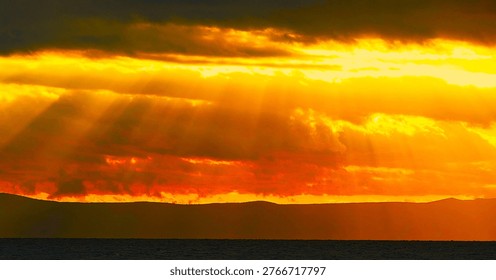 Burning sky with dramatic clouds and divine rays of light above the sea horizon