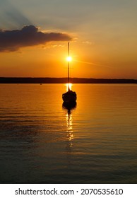 burning sunset at lake Ammersee in Herrsching with a sailing boat resting on the water on a warm August night (Bavaria, Germany)	                               