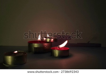 Burning tea light candles casting dramatic shadows on the wall in a dark room.