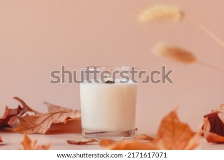 Burning vanilla candle on beige background. Warm aesthetic autumn composition with and dry leaves and flowers. Home comfort, spa, relax and wellness concept. Interior decoration