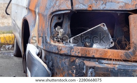 Burnt car body. Arson, short circuit. The skeleton of a burnt car. Front view of a burnt and abandoned rusty van and a broken headlight