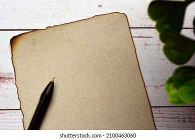 Burnt Edge Brown Paper With Pen On Wooden Desk. Blank For Text