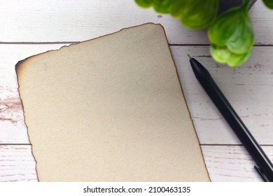 Burnt Edge Brown Paper With Pen On Wooden Desk. Blank For Text