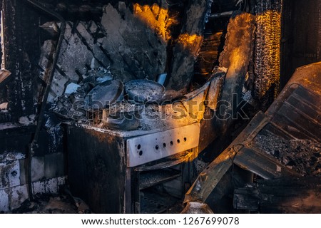 Burnt house interior. Burned kitchen, remains of stove and furniture in black soot.